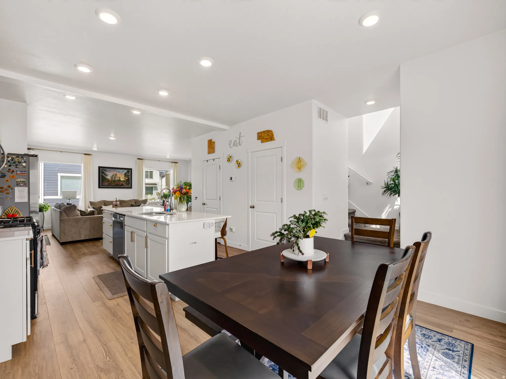 Open-concept living space featuring wood-finish flooring, recessed lighting, a kitchen island with seating, and white cabinetry