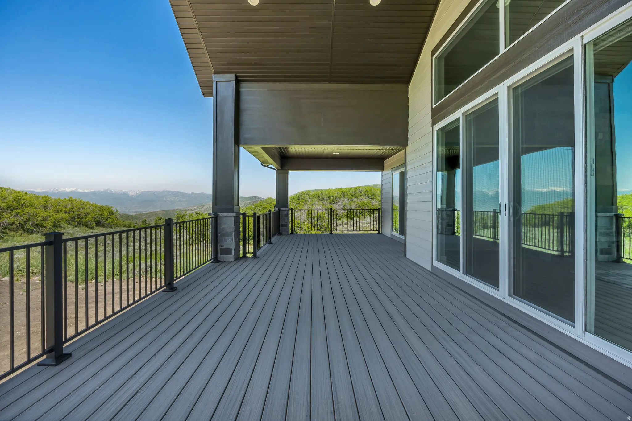 Expansive covered deck with composite decking, black metal railings, and multiple sliding glass doors