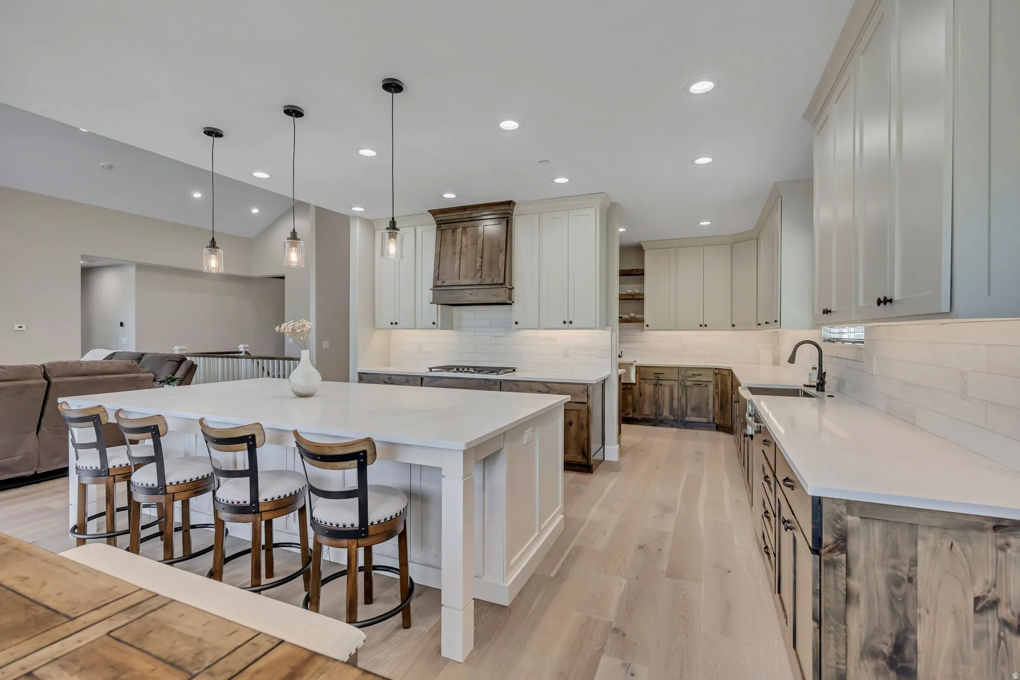 Expansive kitchen featuring a large island, wood-finish flooring, white countertops, subway tile backsplash, and a mix of light and dark wood cabinetry
