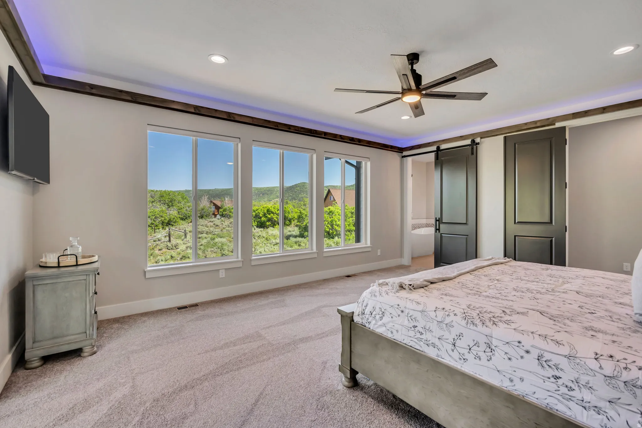 Expansive windows, ceiling fan with integrated lighting, recessed ceiling lighting, and sliding barn doors