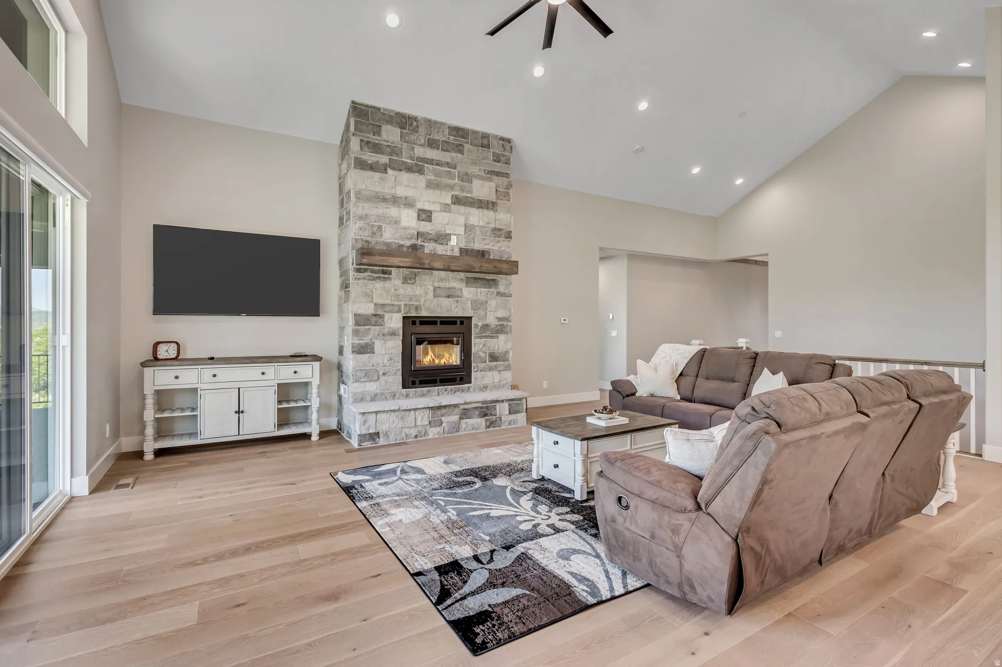 Vaulted ceilings, wood-finish flooring, stone fireplace with hearth, wood mantel, and recessed lighting