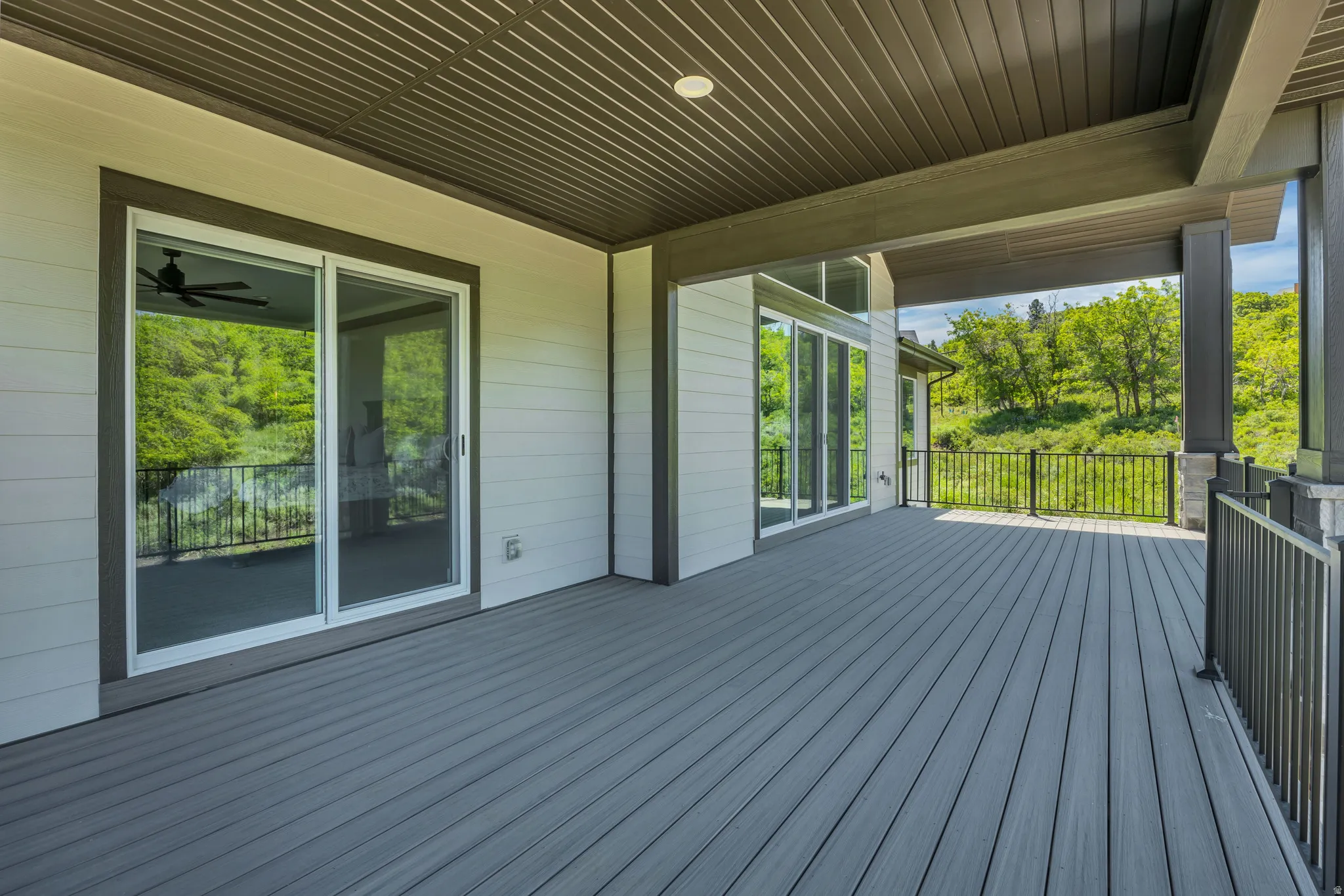 Expansive covered deck featuring composite decking, white siding, and black metal railings