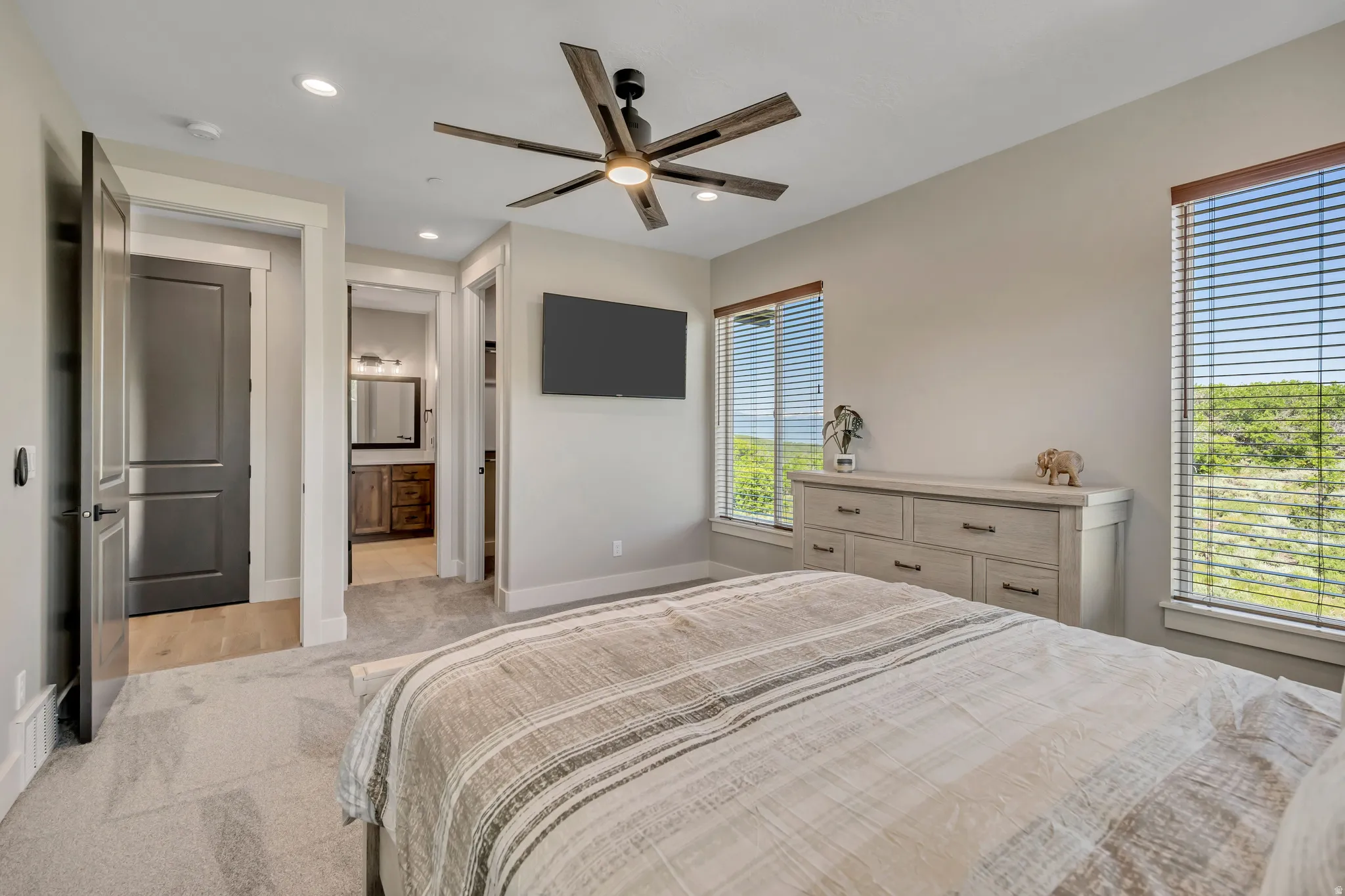 Recessed lighting, wood-finish ceiling fan, wall-mounted television, windows with blinds, and light-colored carpeting