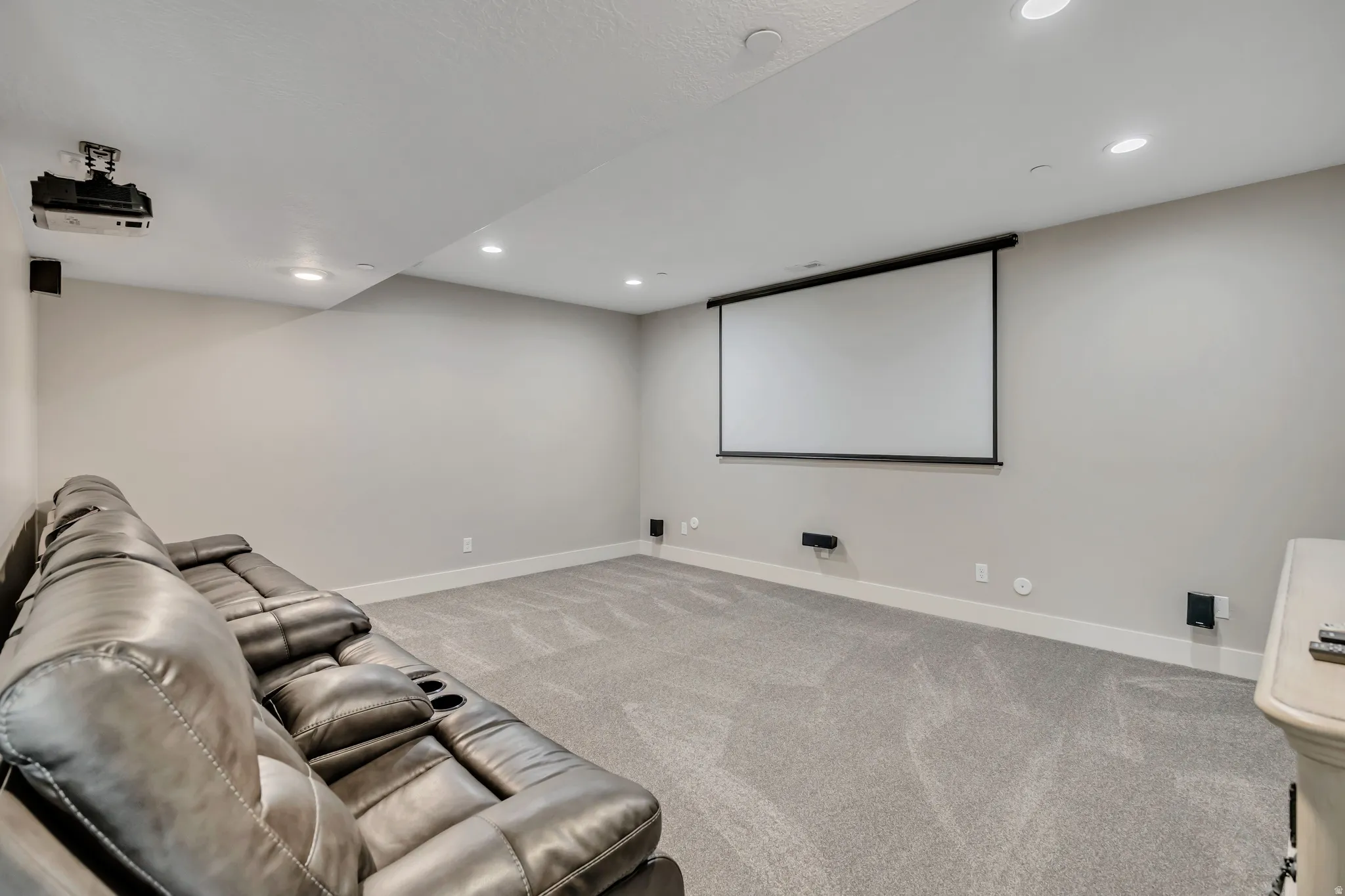 Dedicated media room featuring a large projection screen, mounted projector, recessed lighting, and soft gray carpeting