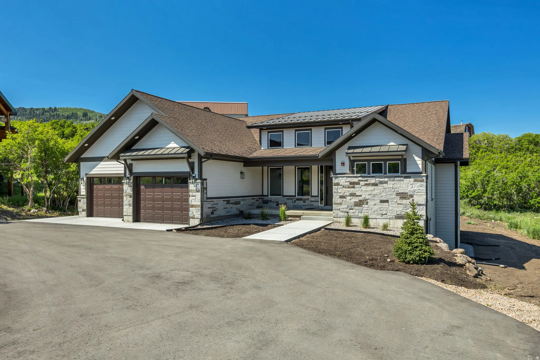 Contemporary residence featuring a multi-tone exterior, two-car garage with dark wood-finish doors, stone accents, and a paved driveway