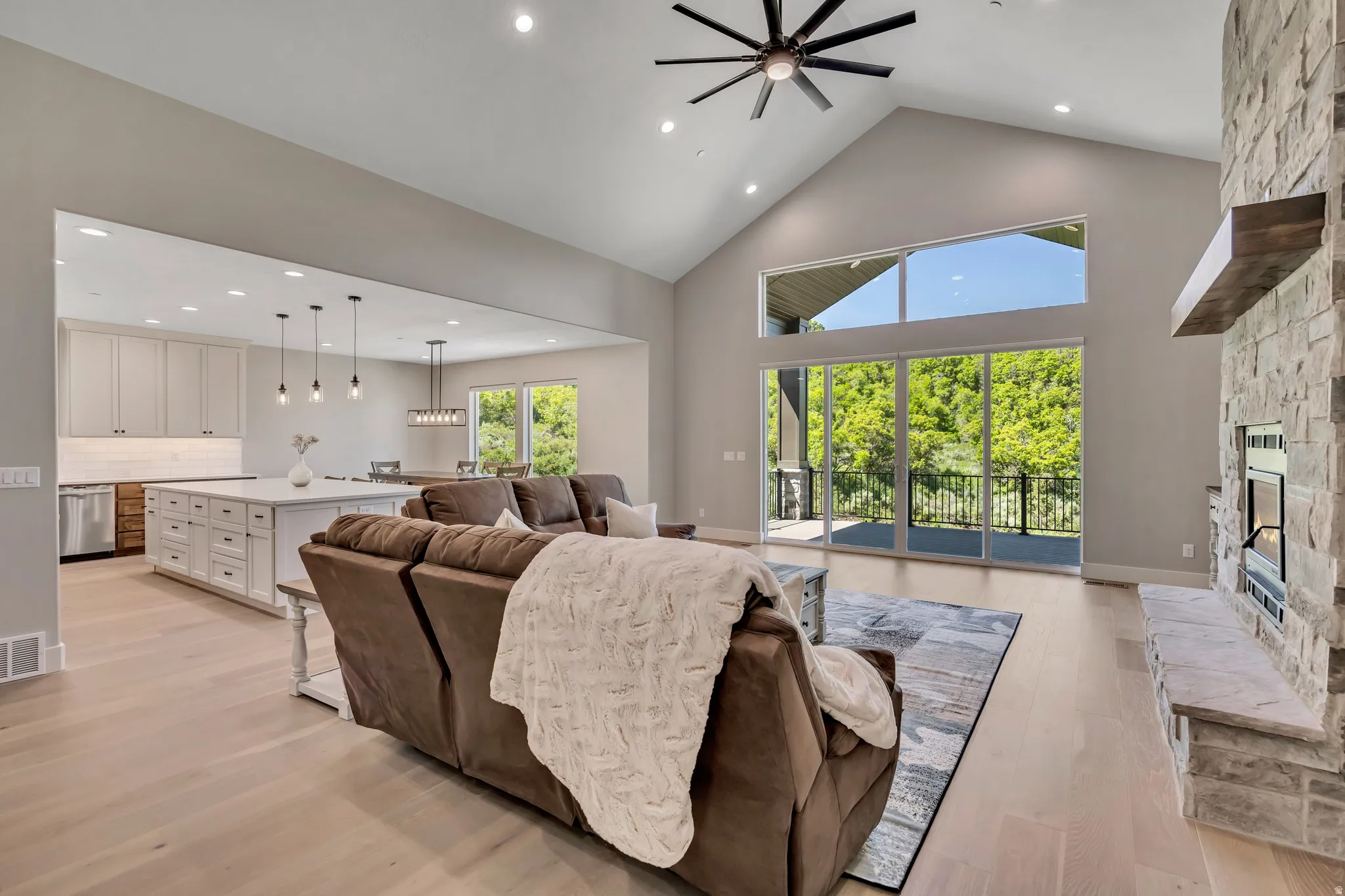 Spacious living area featuring a vaulted ceiling with an exposed beam, a stone fireplace with a wood-finish mantel, and large sliding glass doors leading to an exterior balcony