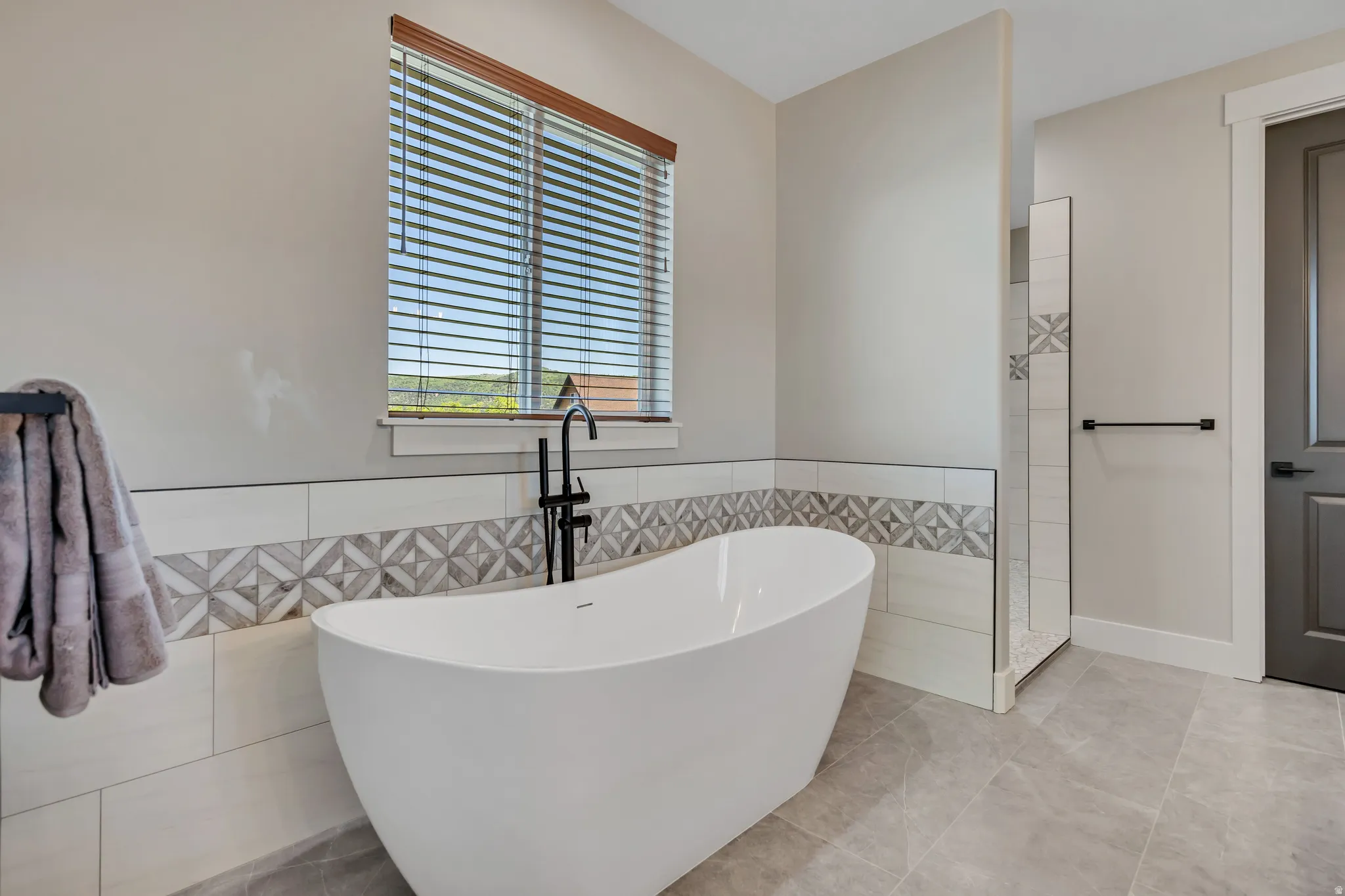Freestanding soaking tub with a black floor-mounted faucet, complemented by a tiled accent wall and an adjacent shower enclosure
