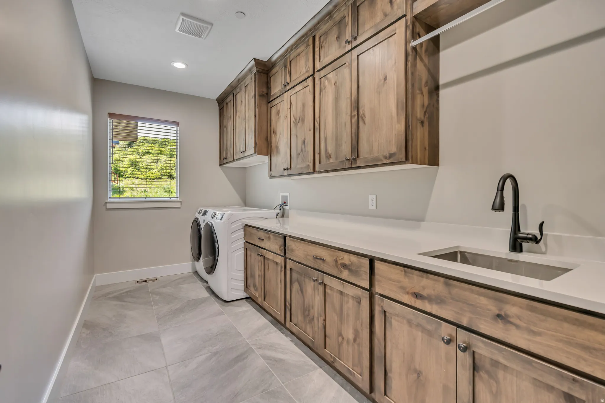 Extensive wood-finish cabinetry, light-toned countertops, and a stainless steel sink with a dark-finish faucet