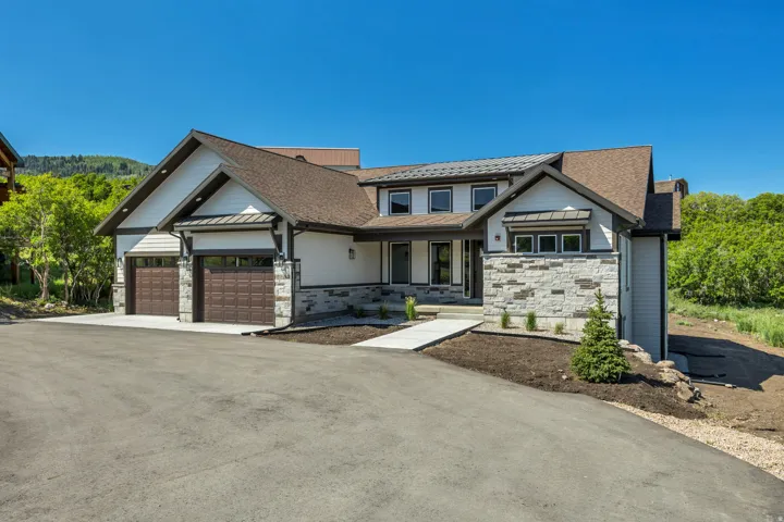 Contemporary residence featuring a multi-tone exterior, two-car garage with dark wood-finish doors, stone accents, and a paved driveway