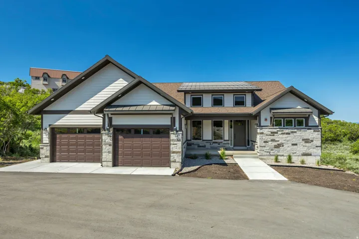 Contemporary exterior featuring stone accents, siding, a prominent front entry, and multiple garage doors