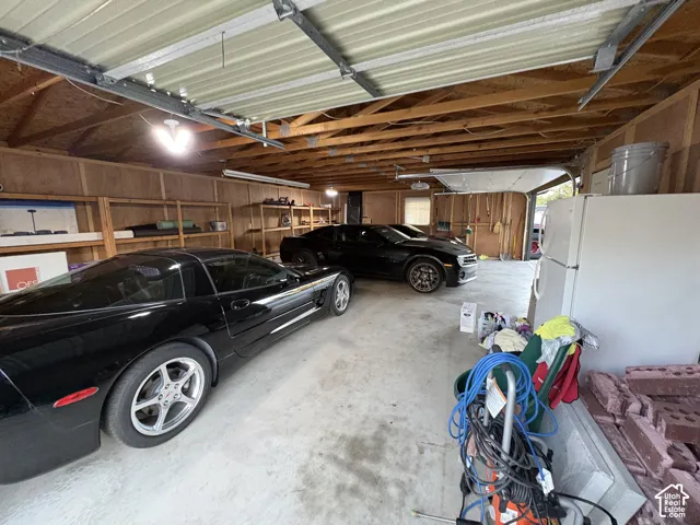 Expansive garage with exposed wood beam ceiling, concrete flooring, and built-in shelving