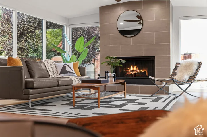 Floor-to-ceiling windows, wood-finish flooring, a tile-surround fireplace, and a ceiling fan