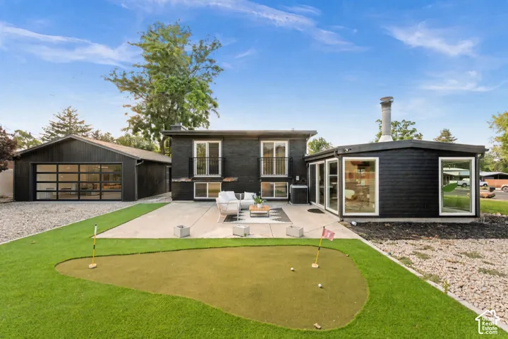 Contemporary exterior with black horizontal siding, expansive concrete patio, putting green, large detached garage with glass panel doors, and multiple large windows