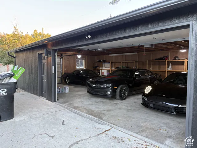Three-car garage with overhead lighting, wood-paneled walls, built-in shelving, and a side access door