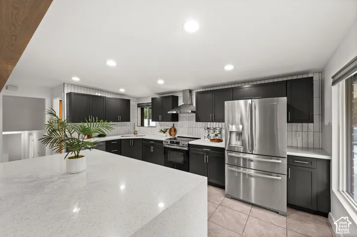 Kitchen featuring dark cabinetry, light countertops, a stainless steel refrigerator, a stainless steel range with hood, and a tile backsplash