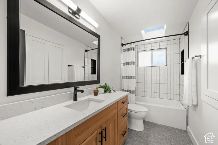 Bathroom featuring a wood-finish vanity with an integrated sink, a speckled countertop, and a black-framed mirror