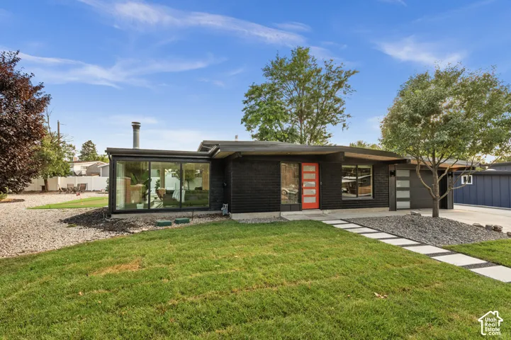 Mid-century modern exterior with dark brick facade, full-light red entry door, horizontal garage door panels, and a concrete paver walkway