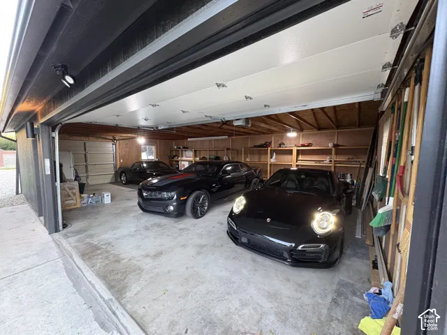 Two-car garage featuring exposed wood framing, concrete flooring, built-in shelving, and overhead lighting