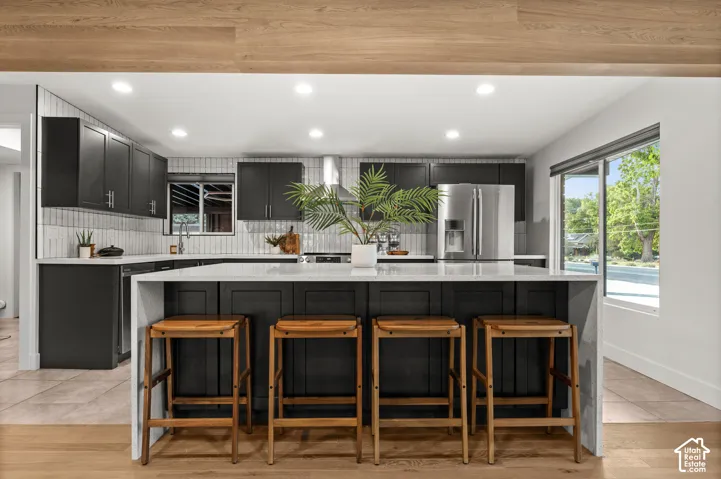 Contemporary kitchen featuring dark cabinetry, stainless steel appliances, a center island with countertop seating, and recessed lighting