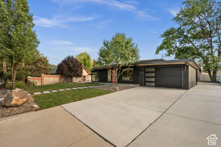 Modern architectural facade with a dark exterior, a red entry door, a multi-paneled garage door, a concrete driveway, and a landscaped front yard with stepping stones