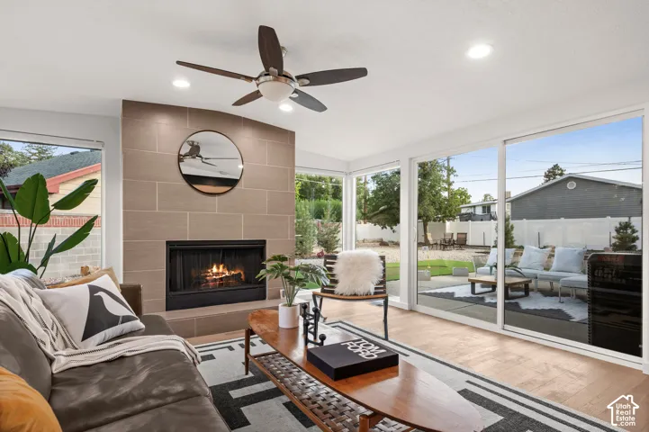 Expansive window wall with outdoor access, tiled fireplace, wood-finish flooring, and a ceiling fan