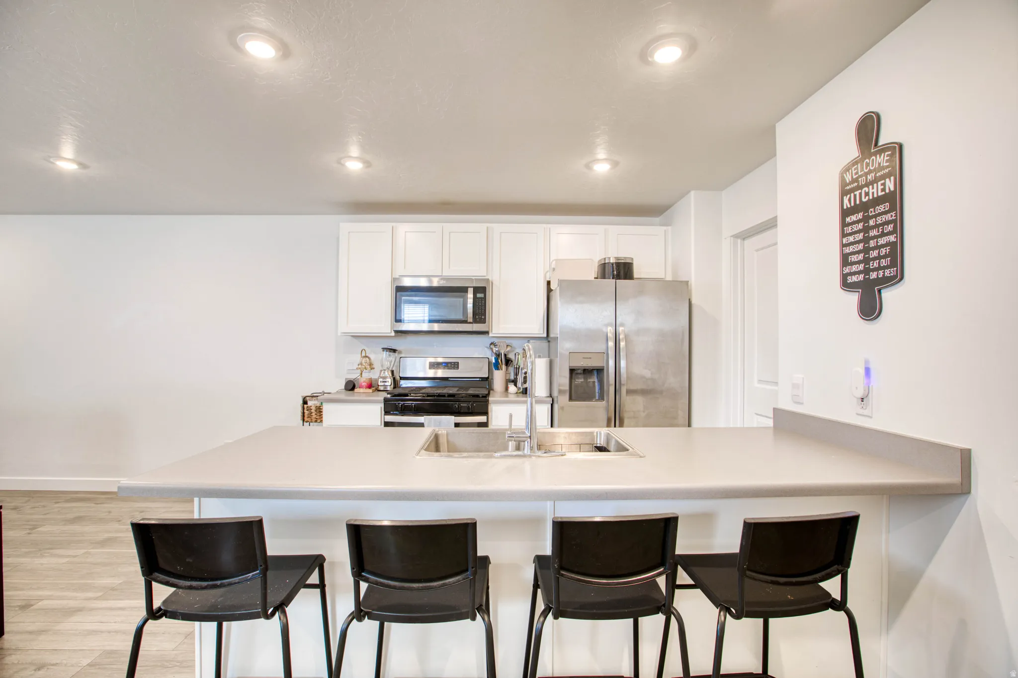 Kitchen featuring a central island with an integrated sink, white cabinetry, stainless steel appliances, and recessed lighting