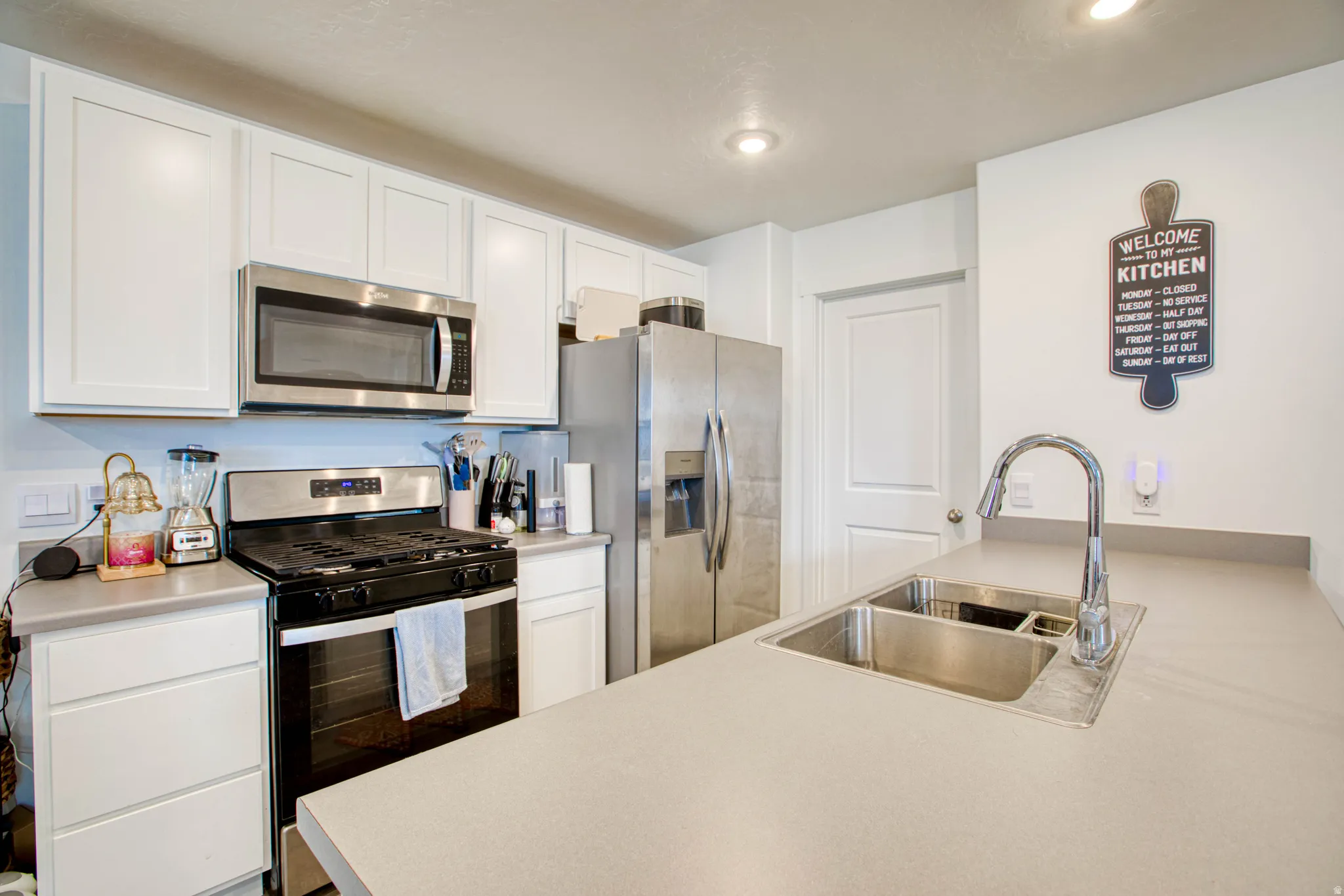 White cabinetry, stainless steel appliances, dual basin sink with gooseneck faucet, light-toned countertops, and recessed lighting