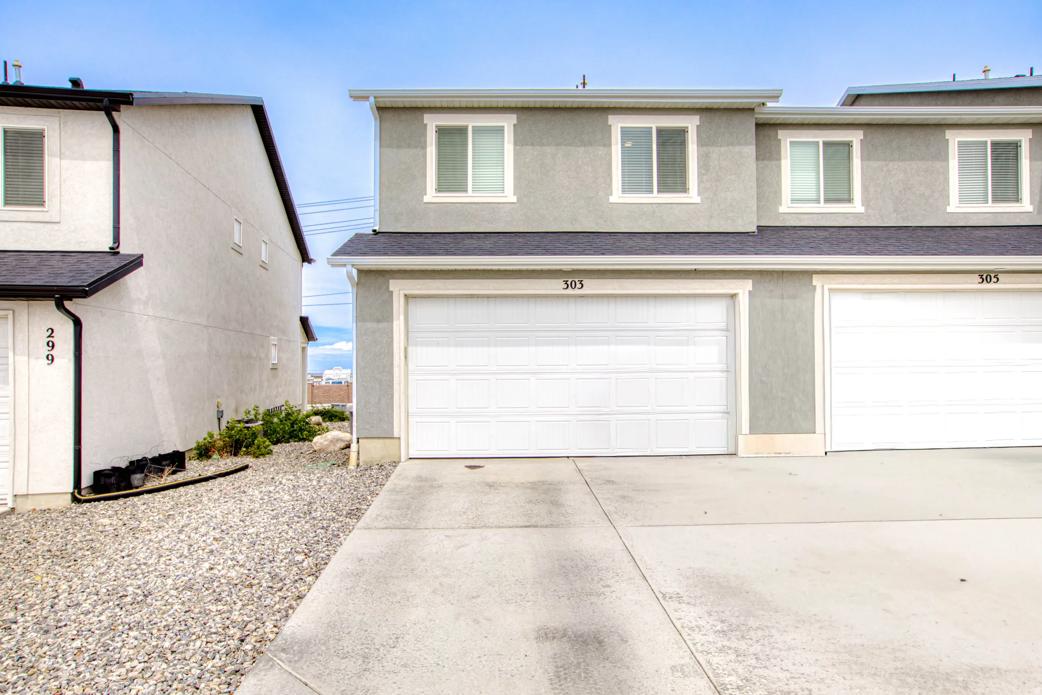 Multi-story exterior with a two-car garage, gray stucco finish, and white-framed windows
