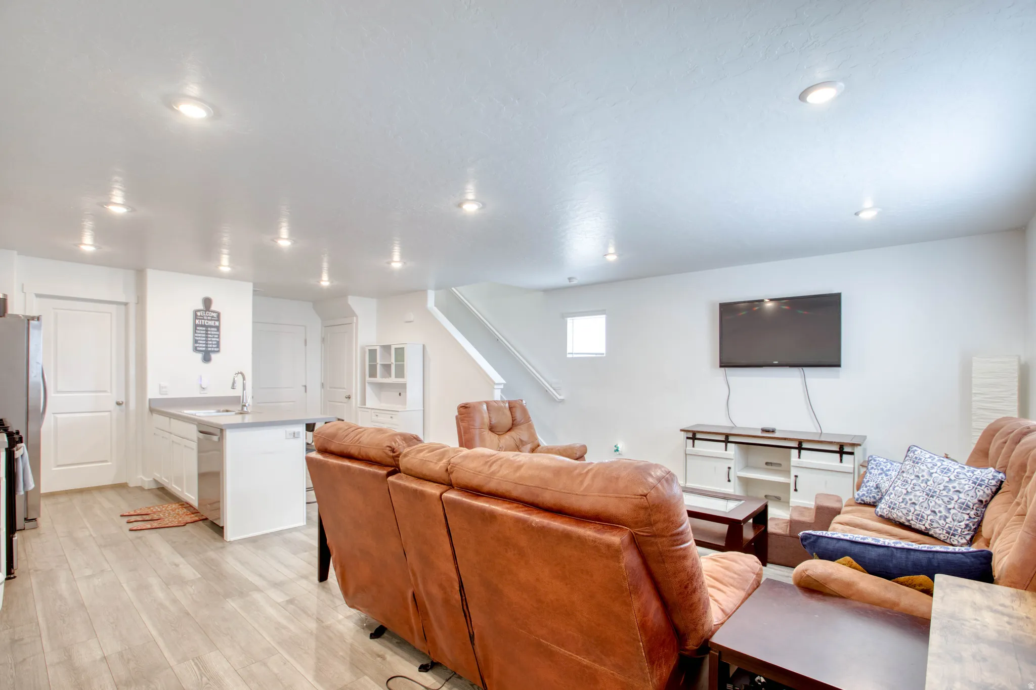 Open-concept living space featuring recessed lighting, light wood-finish flooring, white cabinetry, a kitchen island with sink, and a built-in display cabinet