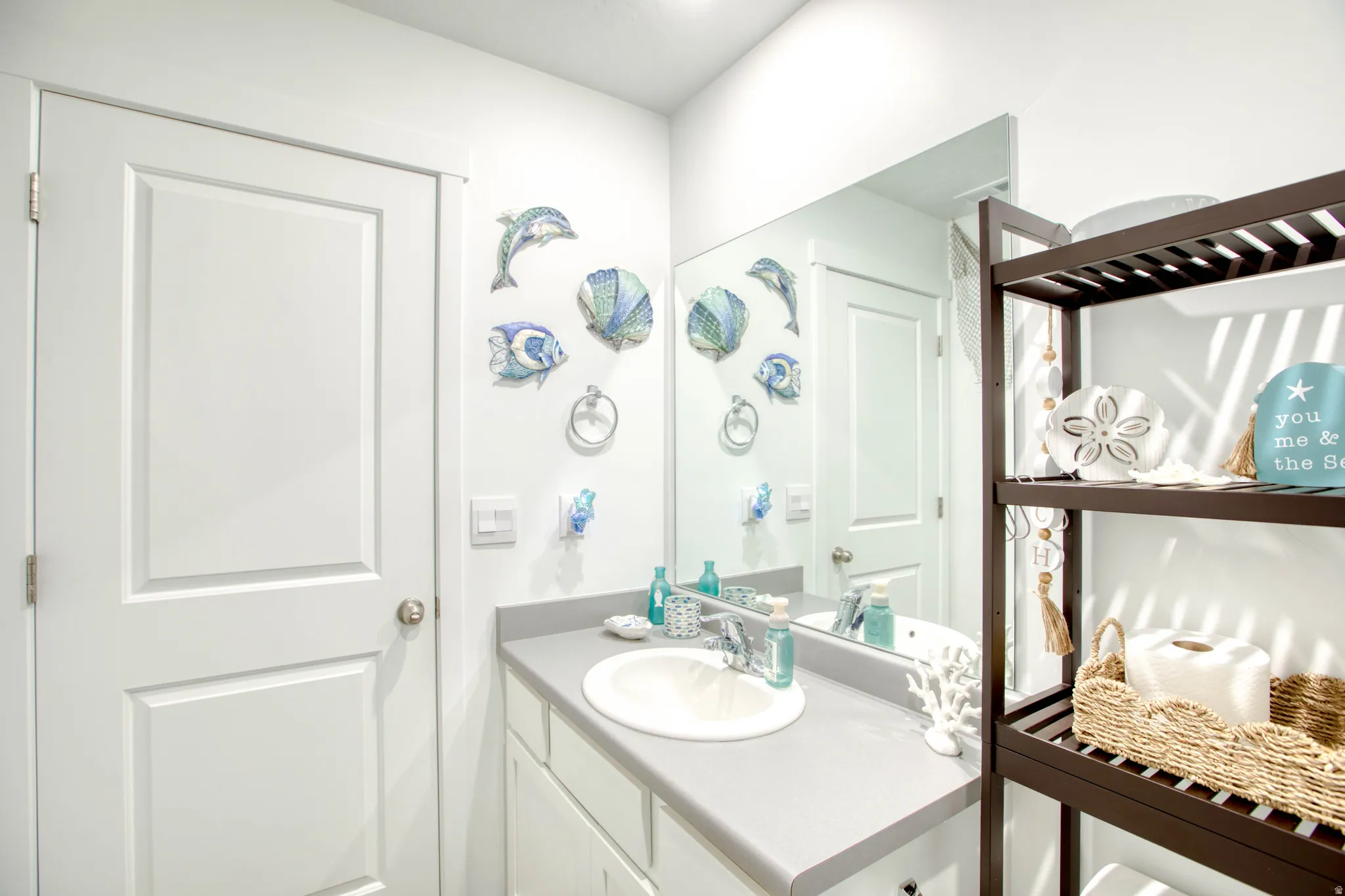 White paneled door, integrated sink, gray countertop, wall-mounted mirror, and dark wood-finish shelving