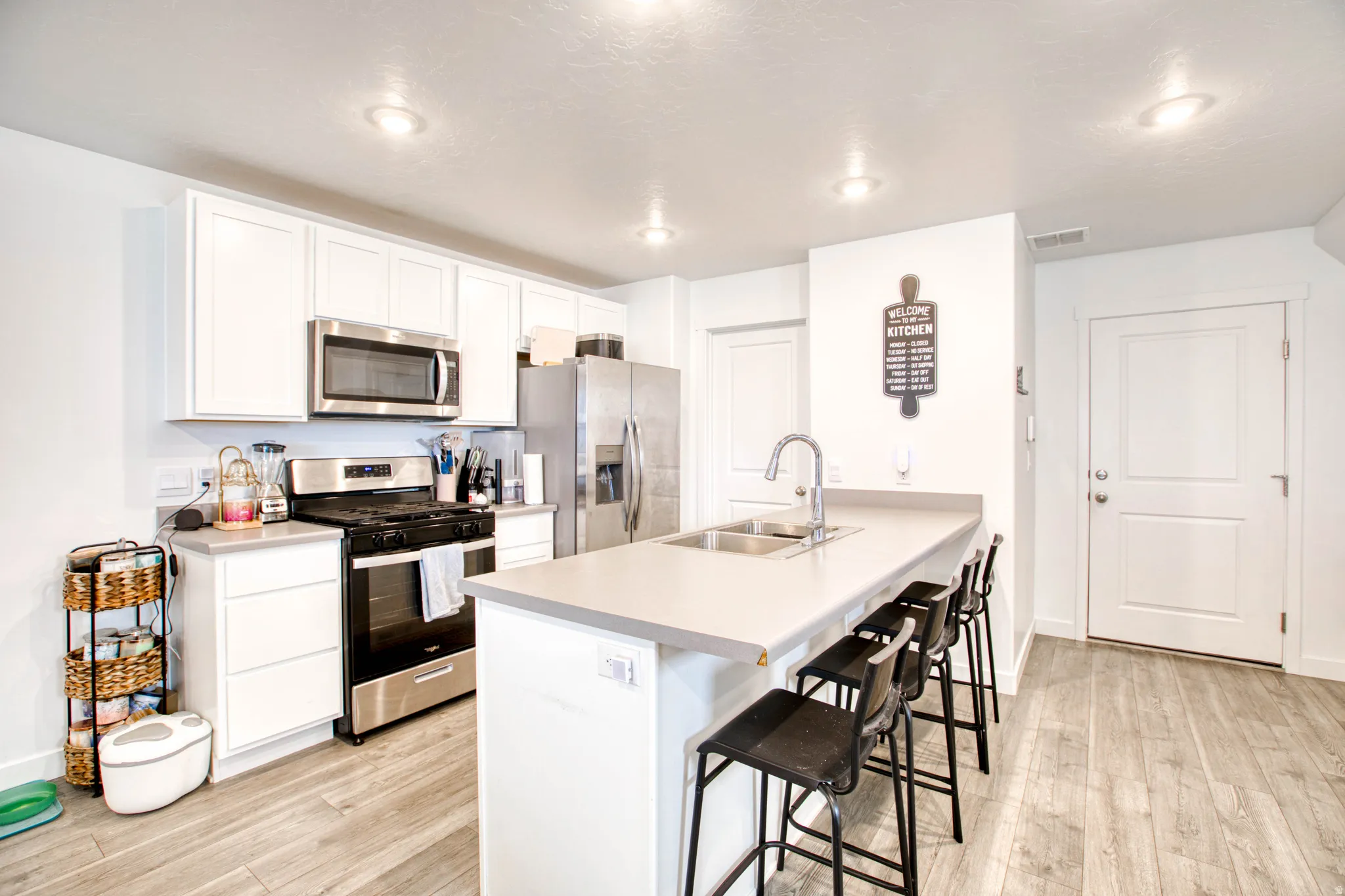 White shaker-style cabinetry, stainless steel appliances, light-toned countertops, and wood-finish flooring