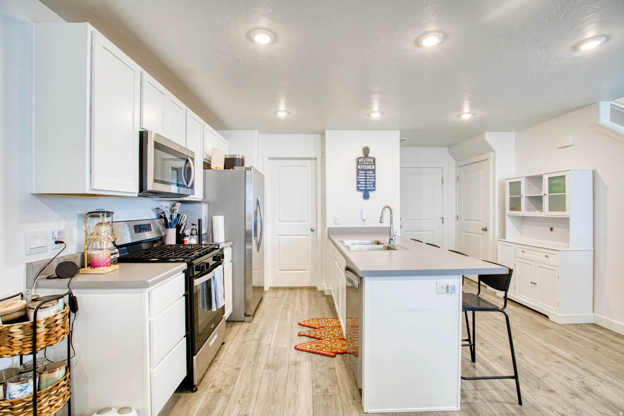 Kitchen featuring light wood-finish flooring, white cabinetry, recessed lighting, stainless steel appliances, and a central island with a sink