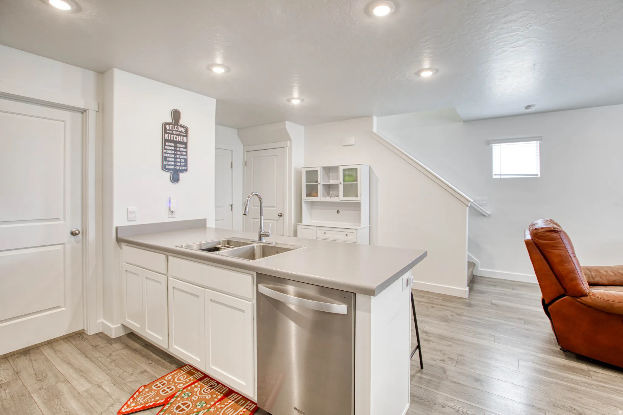 Kitchen island with an undermount dual-basin sink, stainless steel faucet, white shaker cabinetry, and integrated stainless steel dishwasher