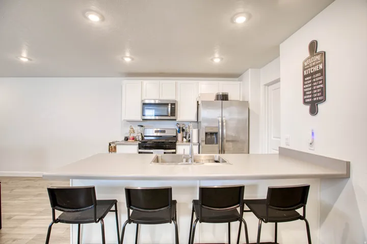 Kitchen featuring a central island with an integrated sink, white cabinetry, stainless steel appliances, and recessed lighting