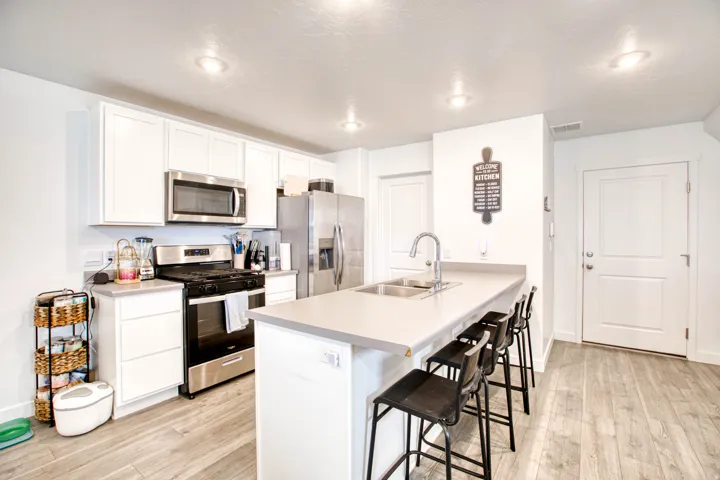 White shaker-style cabinetry, stainless steel appliances, light-toned countertops, and wood-finish flooring