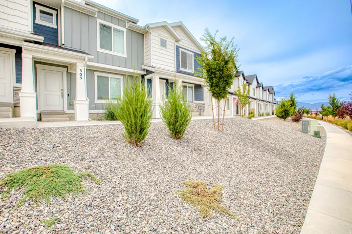 Exterior featuring multi-toned siding, white trim, a covered porch, and a gravel landscape with mature shrubs