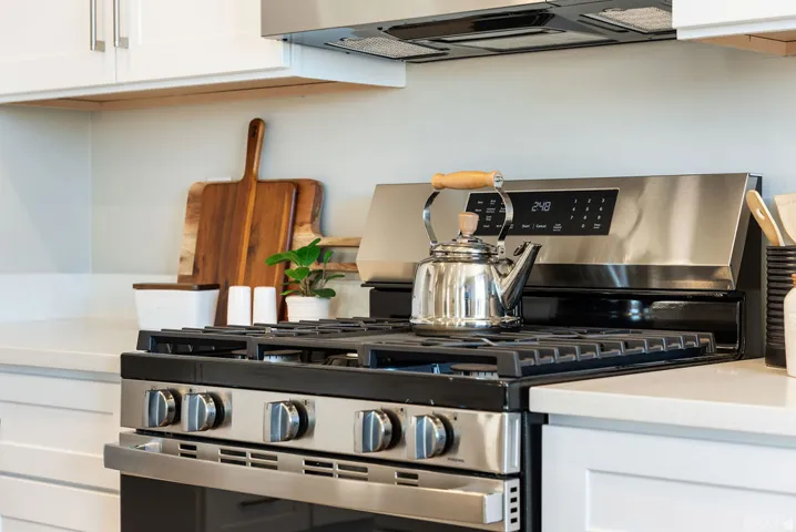 Stainless steel range with gas cooktop, quartz countertop, white shaker cabinetry, and stainless steel range hood
