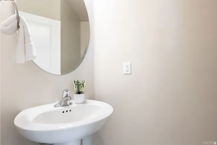 Pedestal sink with chrome-finish faucet, circular wall-mounted mirror, and a wall-mounted towel ring
