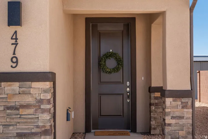 Stucco exterior with stone accents, dark paneled entry door, and exterior sconce lighting