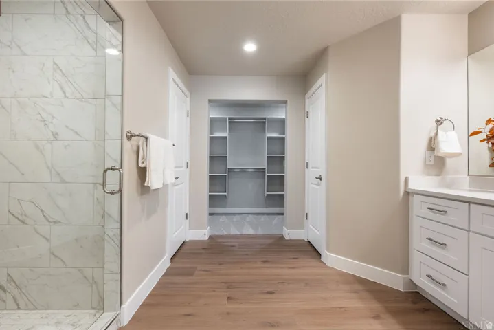 Glass-enclosed shower with large format tile, wood-finish flooring, white vanity with integrated sink, and recessed lighting