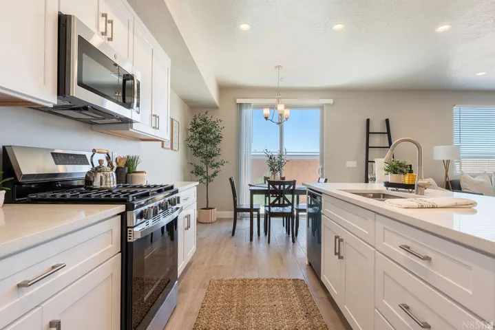 Kitchen featuring white cabinetry, stainless steel appliances, light-toned countertops, and wood-finish flooring