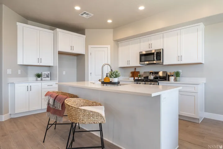 Kitchen featuring white cabinetry, stainless steel appliances, a center island with countertop seating, recessed lighting, and wood-finish flooring