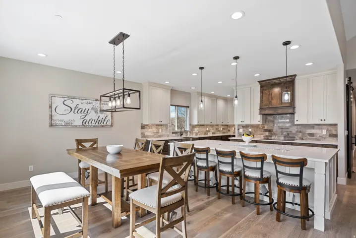 Wood-finish flooring, recessed lighting, a kitchen island with built-in seating, white cabinetry, and a subway tile backsplash