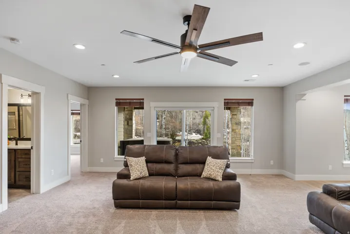 Recessed lighting, wood-finish ceiling fan, sliding glass door, multiple windows, and light-toned carpet