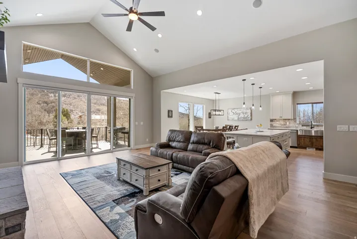 Vaulted ceiling with a ceiling fan and recessed lighting, large glass sliding doors, wood-finish flooring, and an open-concept kitchen with an island and pendant lighting