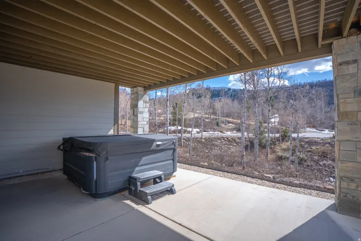 Covered patio with a built-in hot tub, concrete flooring, and stone-clad support pillars