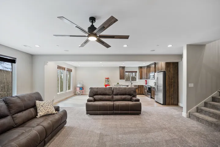 Spacious living area with ceiling fan and recessed lighting, plush carpet, and an integrated kitchen featuring wood-finish cabinetry and stainless steel appliances