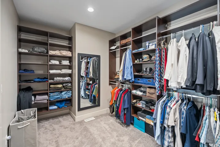 Luxurious walk-in closet featuring custom built-in shelving and cabinetry with polished metal framing, abundant hanging rods for organized wardrobe storage, neutral-toned finishes, recessed lighting, and polished concrete flooring throughout the space