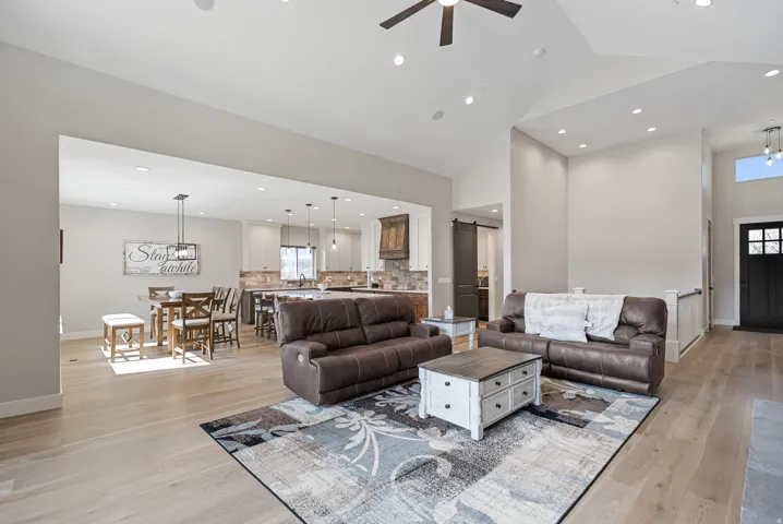 Vaulted ceiling with recessed lighting, wood-finish flooring, open concept layout, modern pendant lighting in kitchen, and a dark-paneled entry door