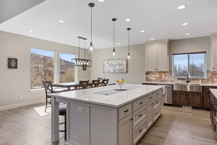 Spacious kitchen featuring a large central island with white countertop, recessed lighting, wood-finish flooring, and a stainless steel farmhouse sink